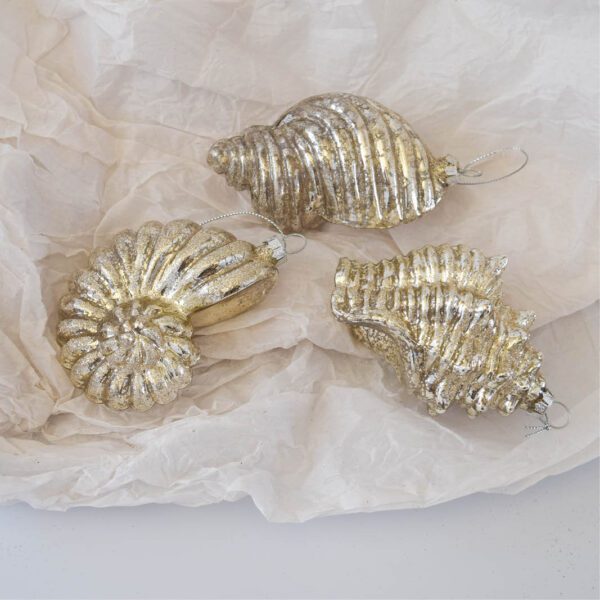 Three silver shell ornaments on a piece of paper.