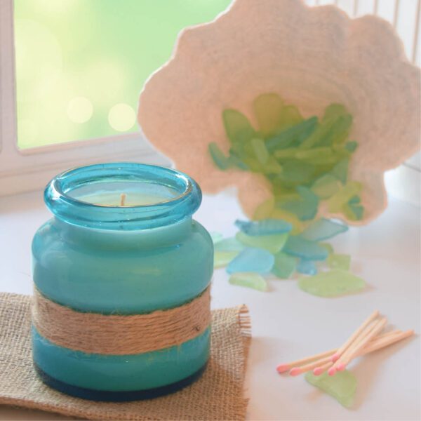 A blue jar with seashells and sand next to it.