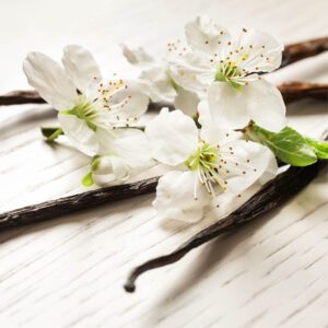 Vanilla blossoms and vanilla pods on a white table.