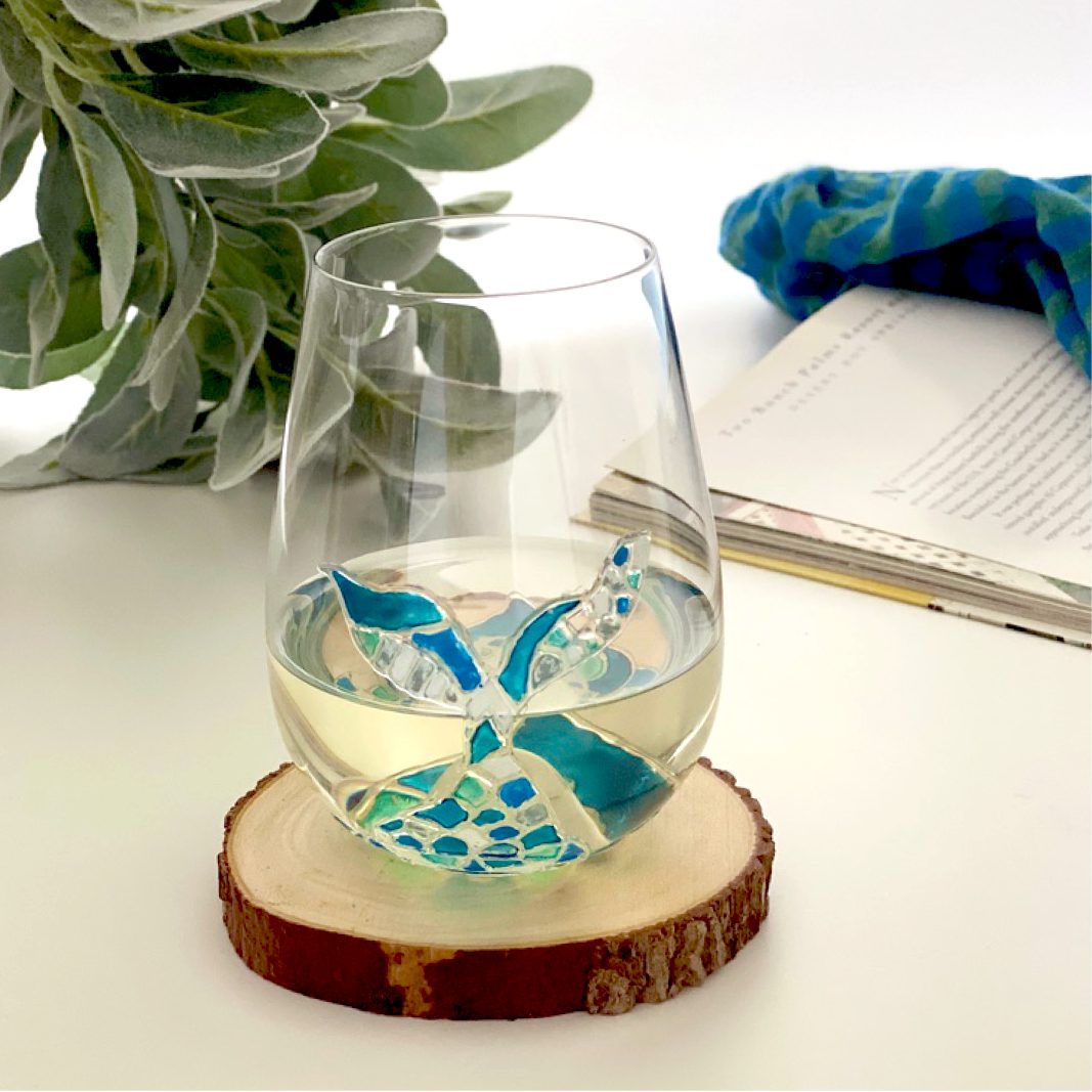 A mosaic wine glass adorned with a delicate blue flower, accompanied by a book resting atop it.