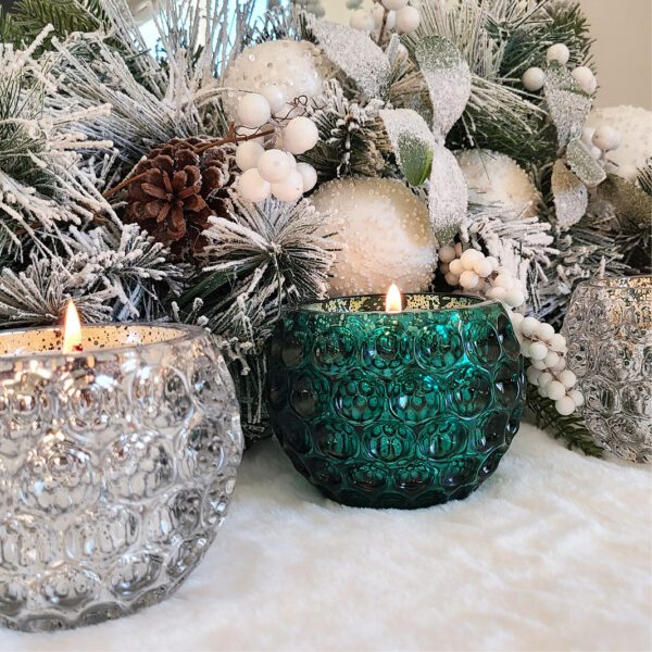 Three glass candle holders in front of a christmas tree.