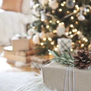 A christmas tree with a gift on top of a furry ottoman.