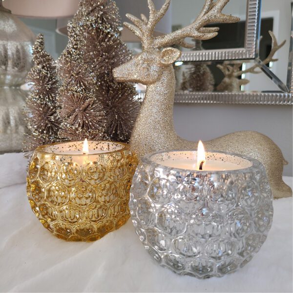 Two gold and silver candles on a table next to a christmas tree.