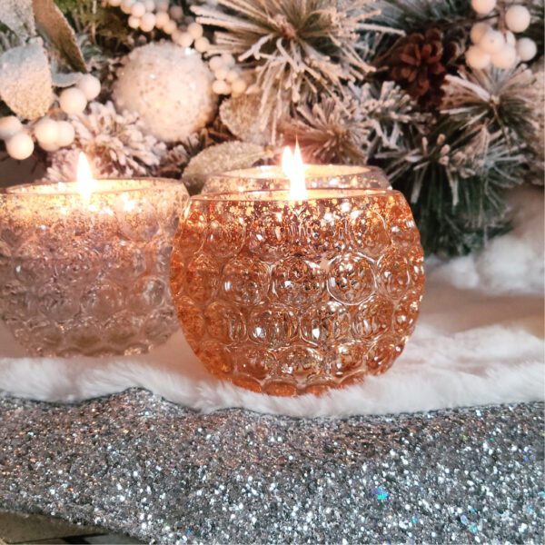 Two candles are sitting on a table in front of a christmas tree.