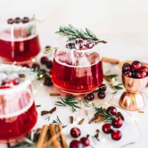 Two glasses of Sparkling Cranberry mulled wine with cinnamon sticks and sprigs of spruce, perfect for the holiday season.