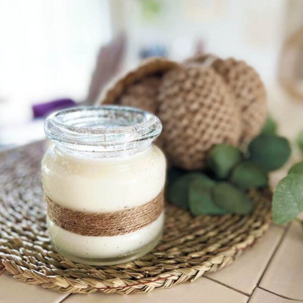 A jar of white candle sitting on a wicker basket.