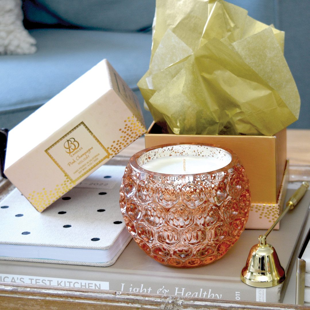 A scented pink candle sits on a tray next to a gold box, adding elegance to your home decor.