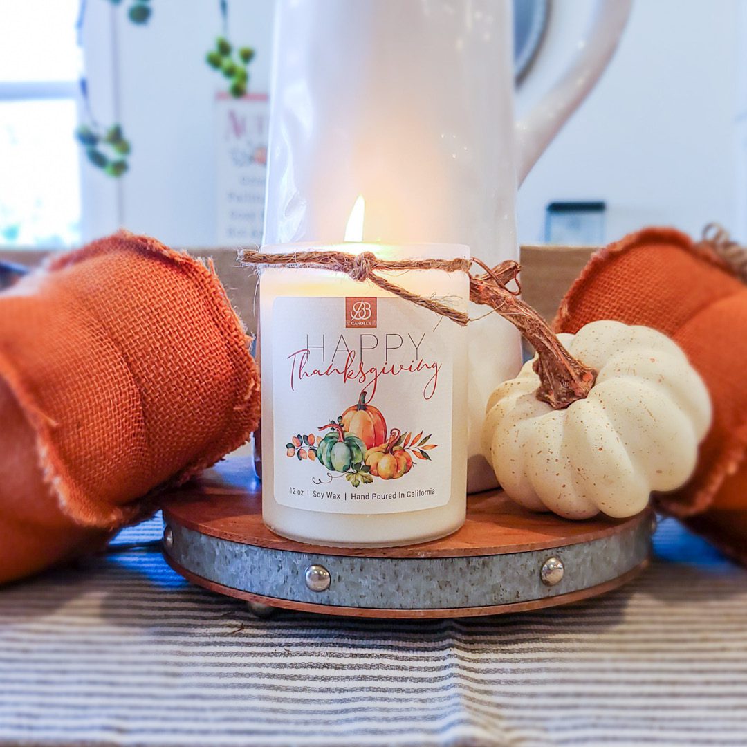 A scented candle sits on a table next to pumpkins, enhancing the home decor.