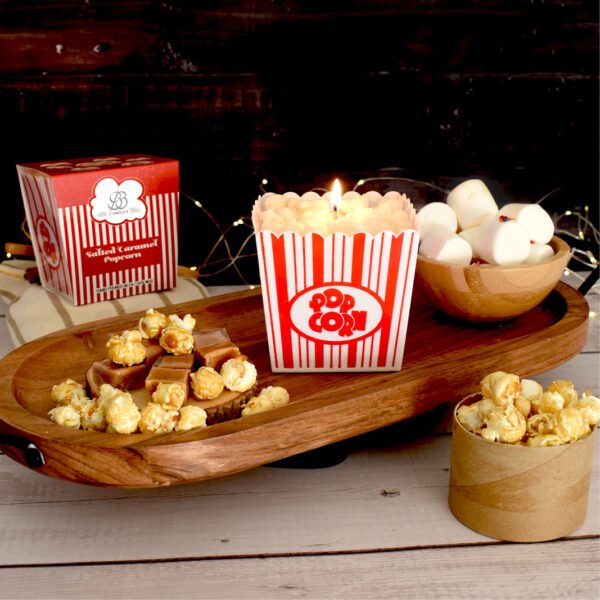 BB Candles salted caramel popcorn candle lit and displayed on a wooden tray with caramel popcorn and chocolate, evoking a cozy ambiance